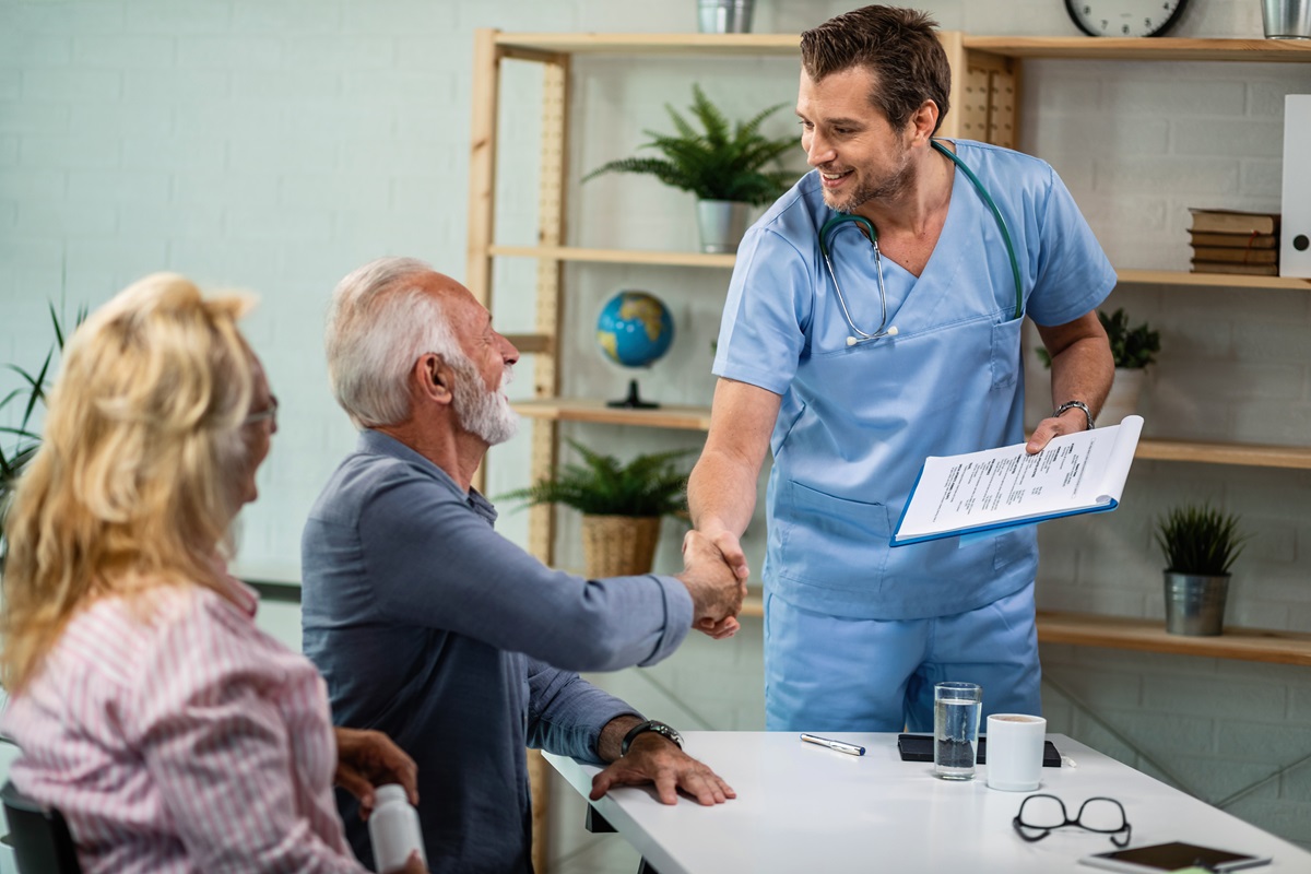 Happy healthcare worker and mature couple greeting at his office. Men are shaking hands.